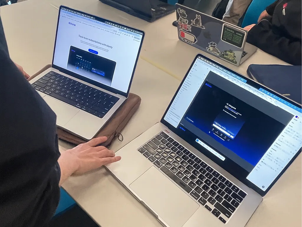 Hackathon setup with two laptops displaying a subscription management dashboard, as developers collaborate side by side.